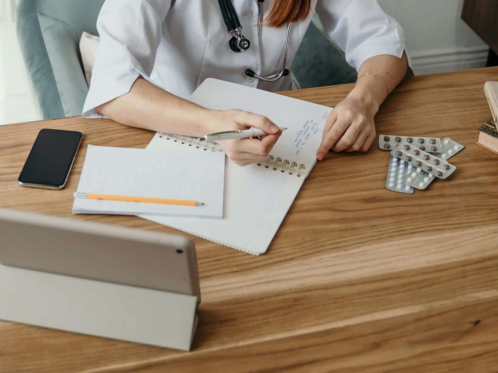 A female doctor writes notes at her desk in a clinical setting, focusing on healthcare tasks.